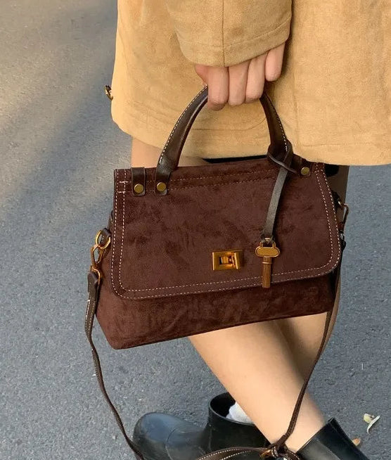 Brown handbag held by a person wearing a beige coat and black boots on a gray background