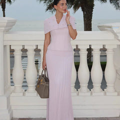 Woman in a light pink dress standing in front of a white railing with palm trees in the background.