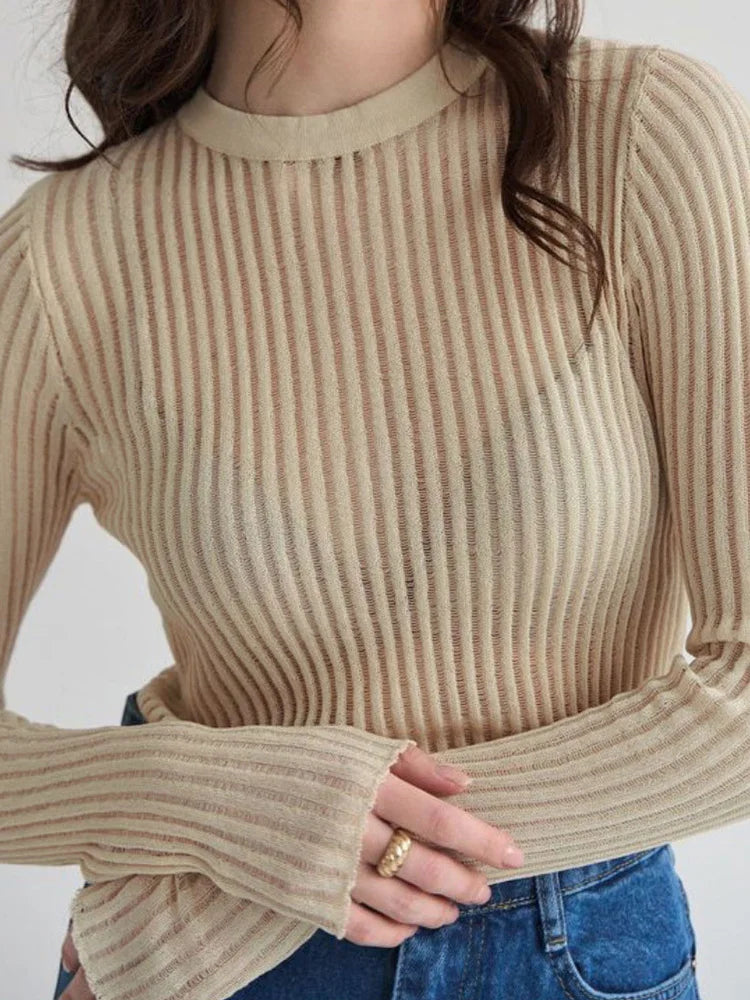 Person wearing a beige ribbed sweater with a plain background
