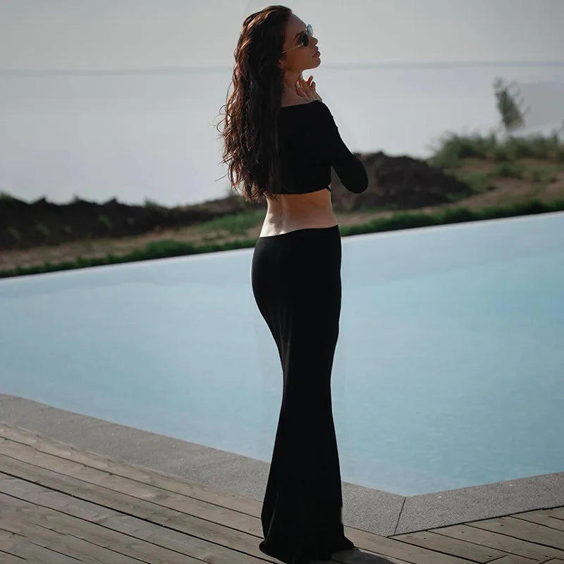 Woman in a black outfit standing by a pool with a scenic background