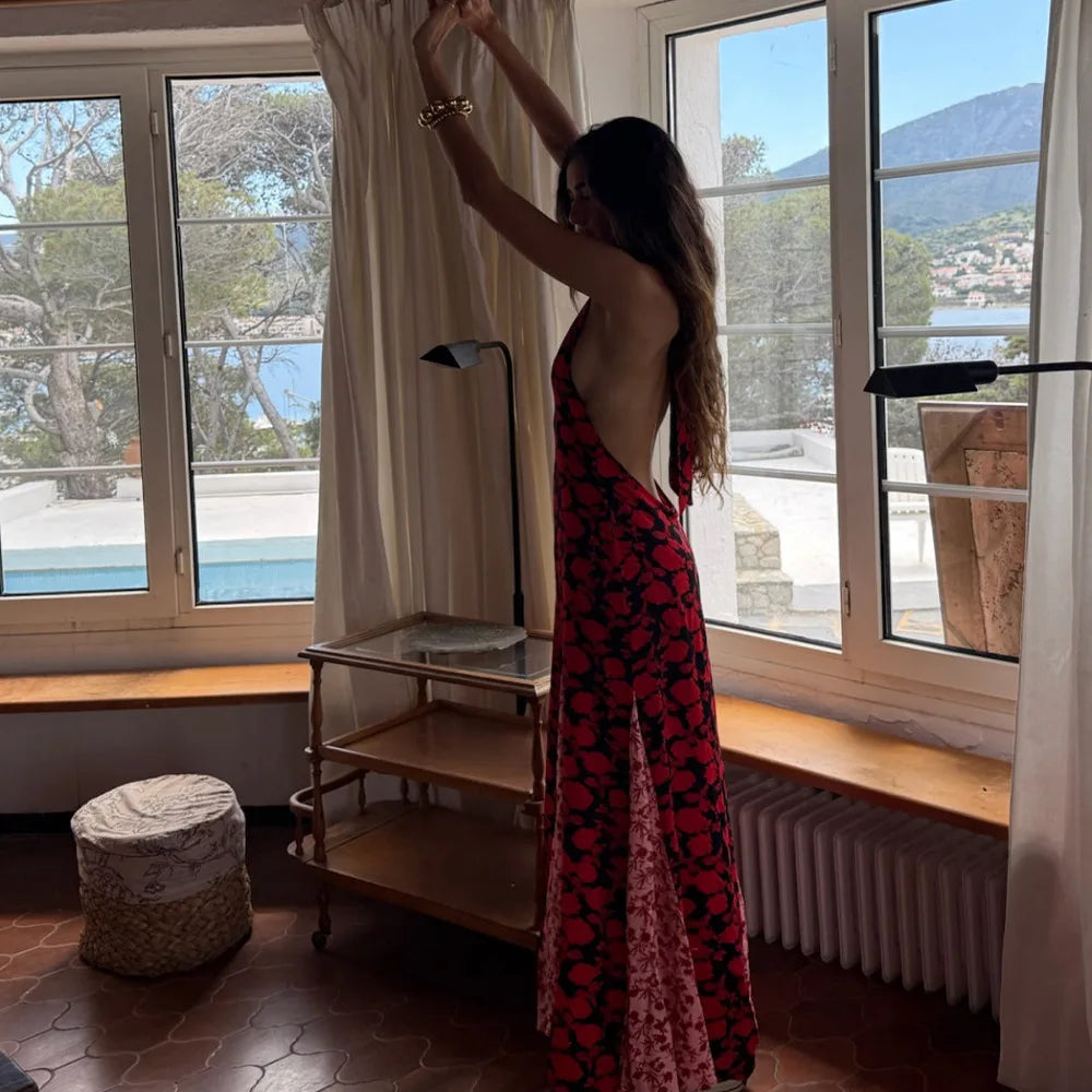 Woman in a red and pink patterned dress standing by a window with a scenic view.
