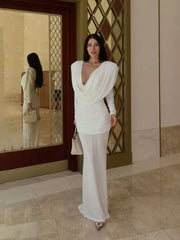 Woman in a white outfit standing in a room with a mirror reflecting her.