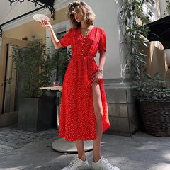 Woman in a red dress standing outdoors with plants and a building in the background
