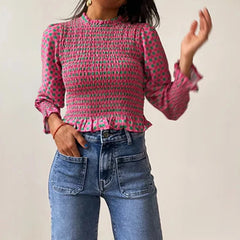 Person wearing a pink patterned blouse and blue jeans against a plain background