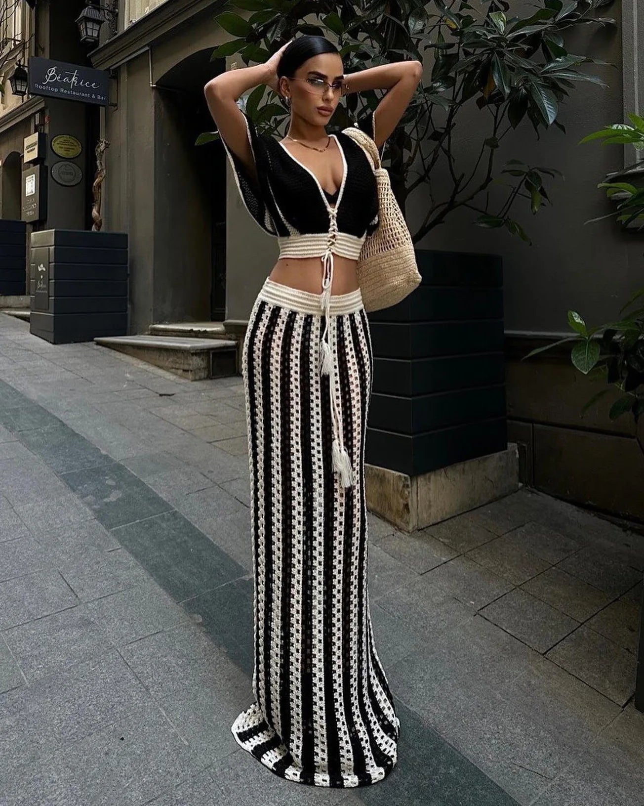 A model wearing a striped knitted dress set with a hollow-out long skirt and a V-neck crop top, posing on a street - Golden Atelier 1