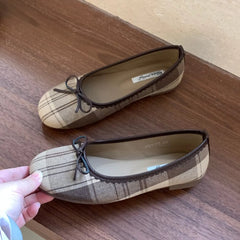 A pair of beige checked ballet flats on a wooden surface