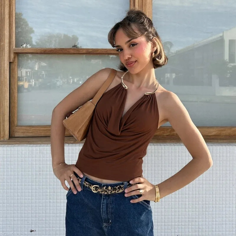 Woman in a brown top and blue jeans standing indoors with a window in the background