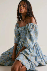 Woman wearing a blue floral dress sitting against a white background