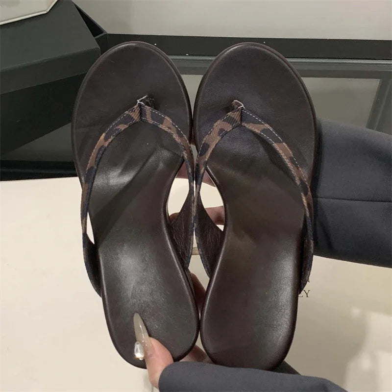 Pair of dark brown sandals being held up with a neutral background
