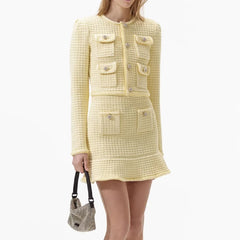 Woman wearing a yellow tweed dress holding a matching handbag on a white background