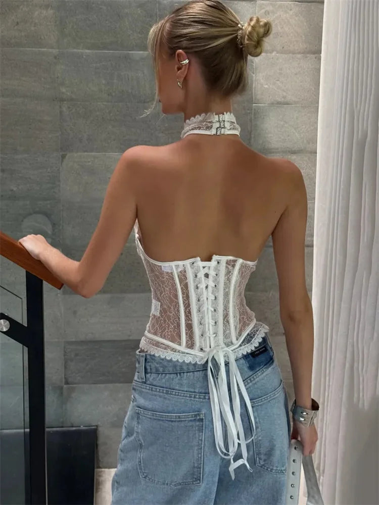 Woman wearing a white lace top and blue jeans in an indoor setting.