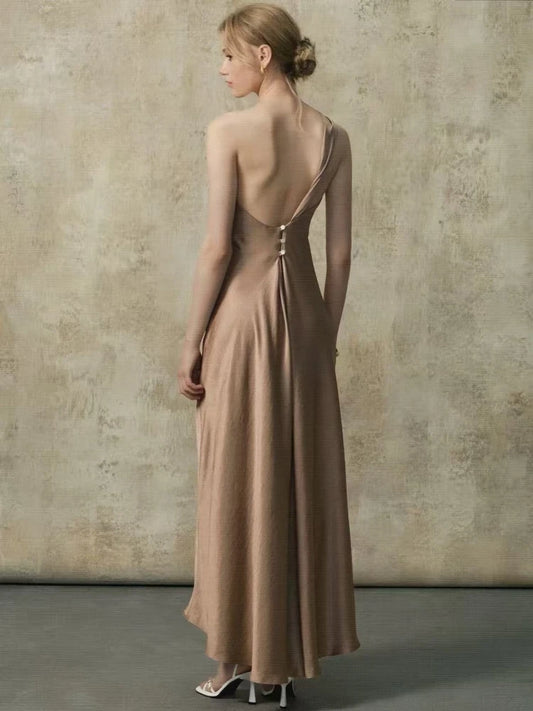 Back view of a woman in a one-shoulder maxi dress showing the open back with buttons