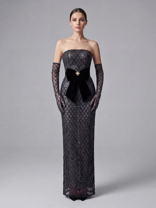Woman wearing a black strapless evening gown with lace detailing on a gray background