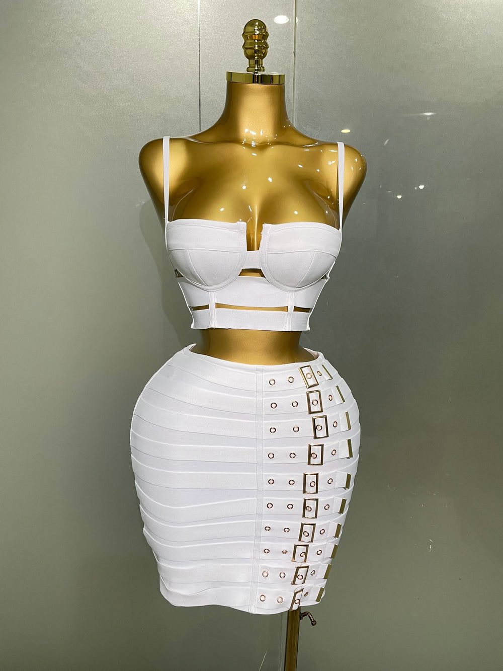 White dress with gold accents on a mannequin against a neutral background