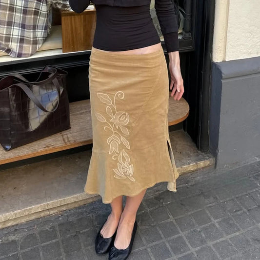 Person wearing a beige skirt with floral embroidery on a street.