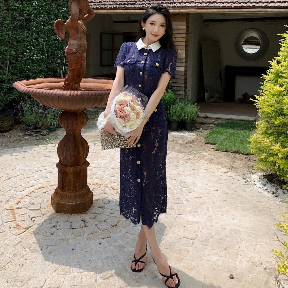 Woman in a navy dress holding flowers and a clutch in front of a stone fountain.