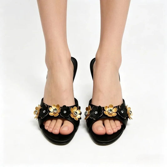 Feet wearing black heeled mules adorned with metal flowers