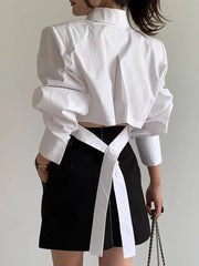 Person wearing a white blouse with long sleeves and a black skirt with a white belt against a plain background