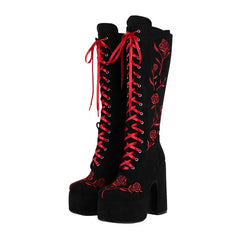 Black knee-high boots with red laces and floral embroidery on a white background