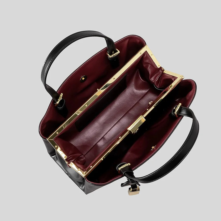 Open view of a black structured top handle bag showing the contrasting red interior and gold clasp.