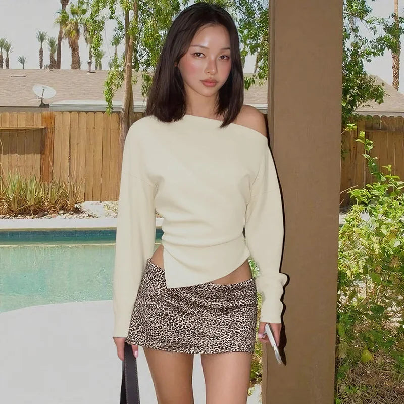 Woman in a cream sweater and leopard print skirt standing by a poolside.