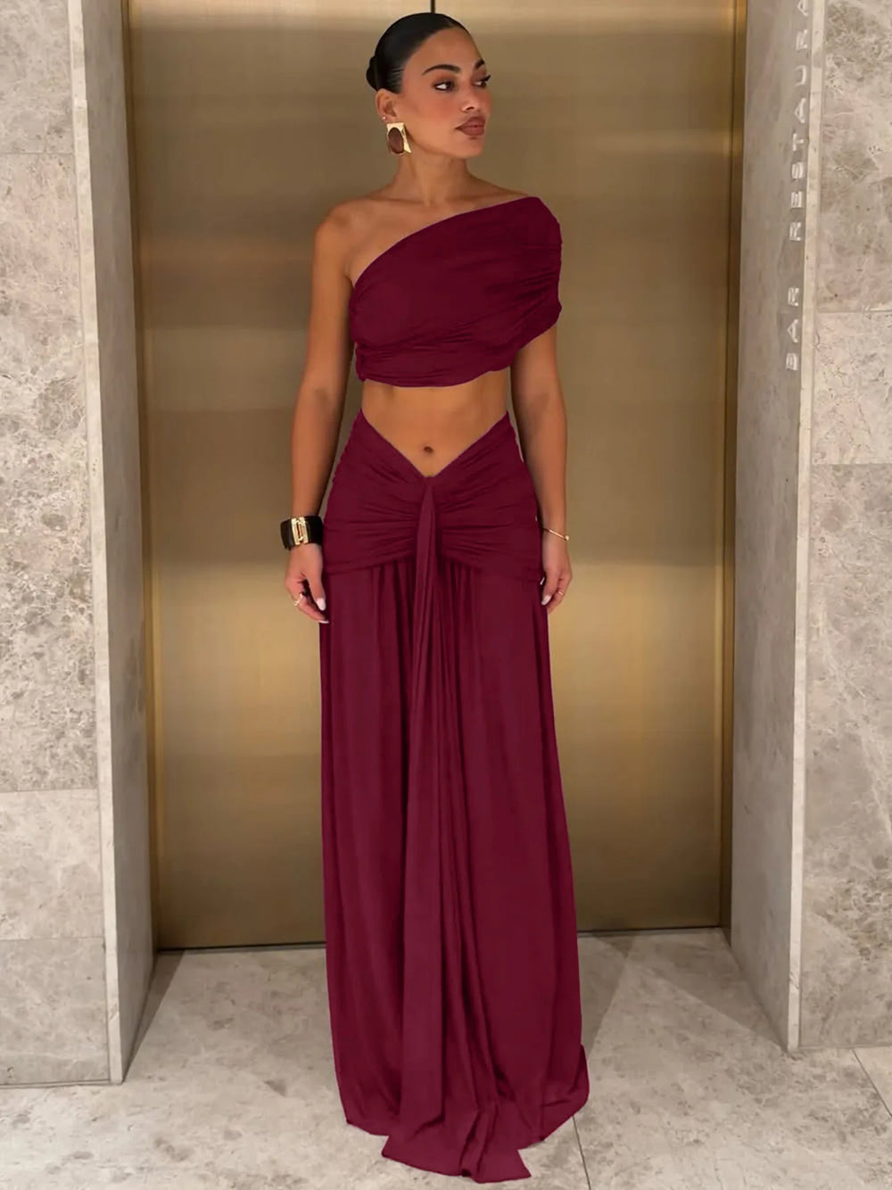 Woman in a burgundy one-shoulder ruched top and flowing maxi skirt