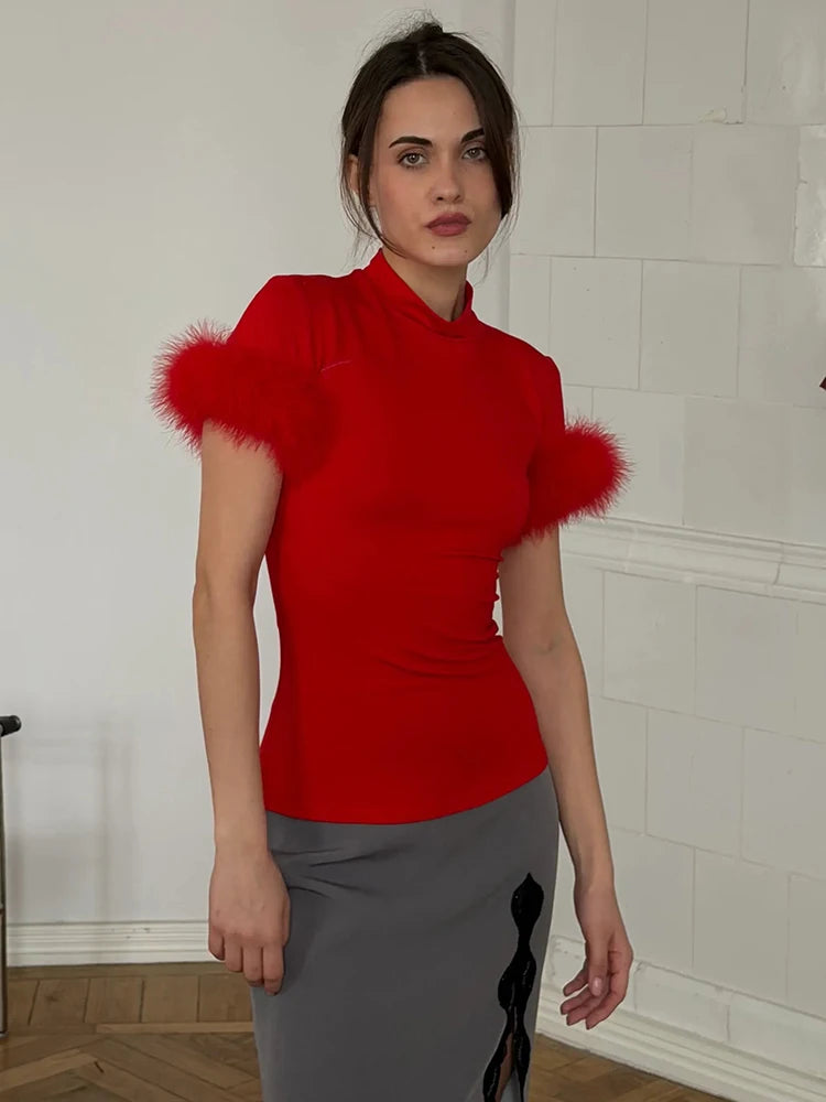 Woman wearing a red top with feathered shoulders against a white wall.