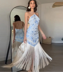 Woman wearing a blue floral one-shoulder dress with white fringe in front of a mirror.