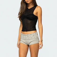 Woman wearing a black top and beige shorts with studs on a light gray background