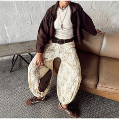 Person wearing a brown jacket, white shirt, and lace pants sitting on a couch.