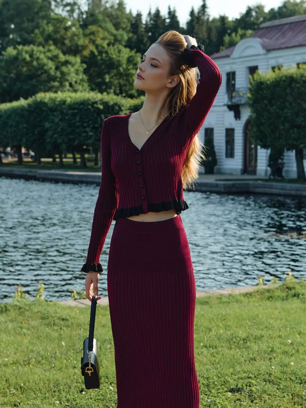 Woman in a burgundy outfit standing by a lake with a building in the background