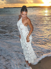 Woman in a white lace dress standing on a beach at sunset