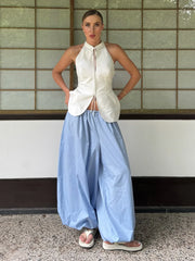 Person wearing a white sleeveless top and light blue wide-leg pants standing against a tiled wall.