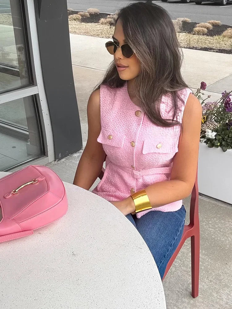 Woman in pink sleeveless top and blue jeans sitting at a table with a pink handbag.