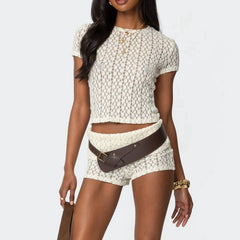 Woman wearing a textured white top and shorts with a brown belt on a light gray background