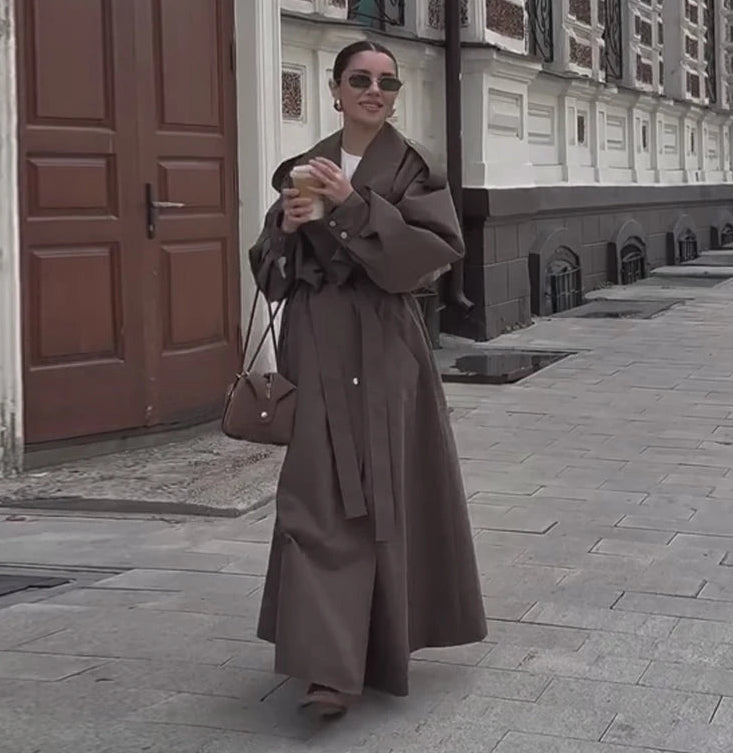 Woman in a long brown coat standing on a street with buildings in the background