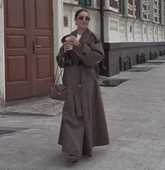 Woman in a long brown coat standing on a street with buildings in the background