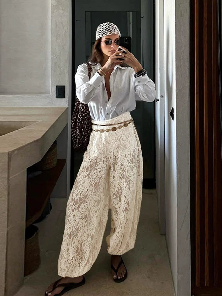Person taking a mirror selfie wearing a white shirt and lace pants in a bathroom.