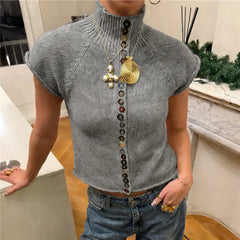 Person wearing a gray sleeveless top with decorative buttons and gold necklace indoors.