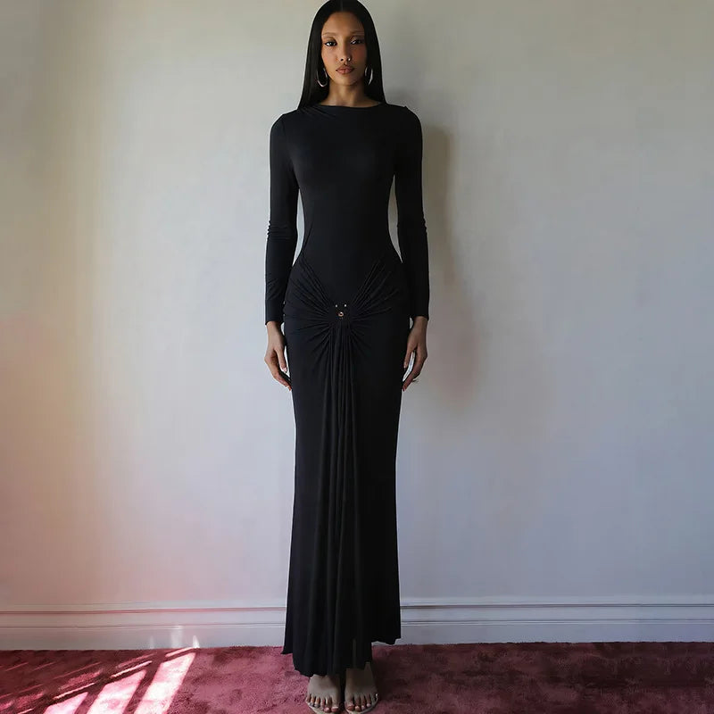 Woman wearing a black dress standing against a plain wall.