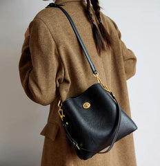 Person wearing a brown coat holding a black handbag with gold accents.