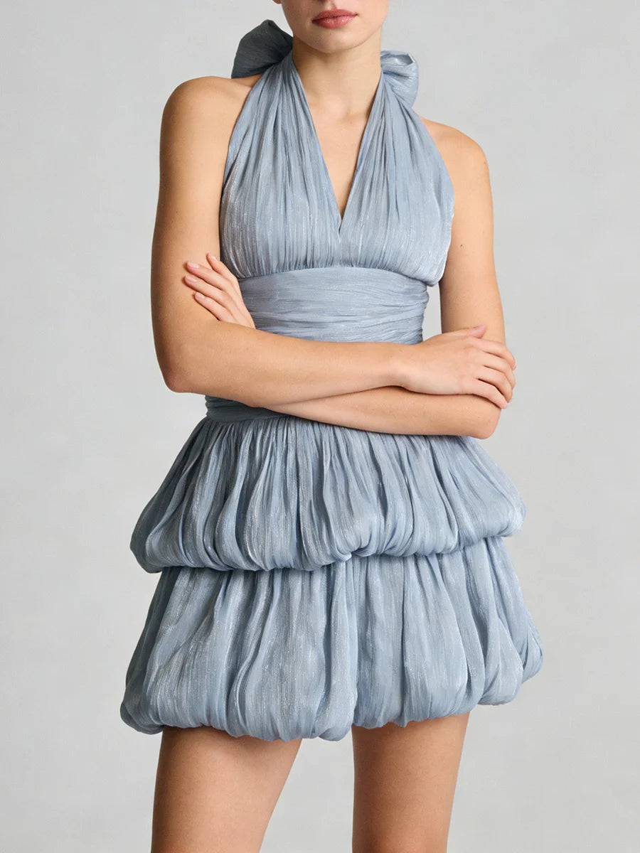 A woman wearing a blue dress with a ruffled skirt on a plain background