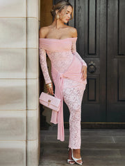 Woman in a pink lace outfit standing against a door.