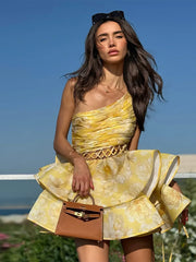 Woman in a yellow dress holding a brown handbag against a blue sky.