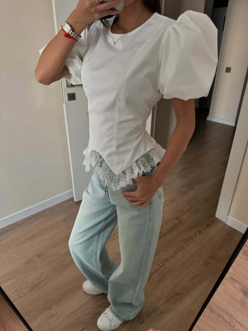 Person wearing a white blouse with puffed sleeves and light blue jeans indoors.