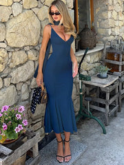 Woman in a blue dress standing against a stone wall with decorative elements.