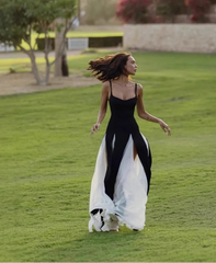 Woman in a black and white dress standing on grass with trees and a horse in the background