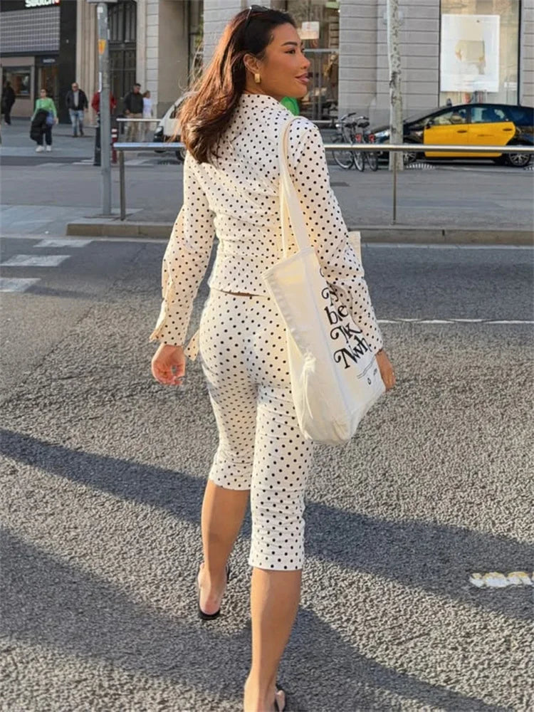 Woman in a polka dot outfit walking on a street with a white tote bag.