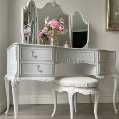 White vanity table with mirror and stool, decorated with flowers, in a room setting.