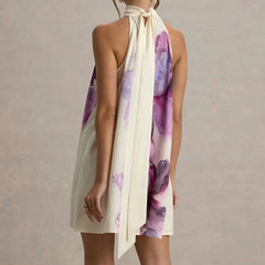 Woman wearing a white halter neck dress with purple floral patterns on a plain background